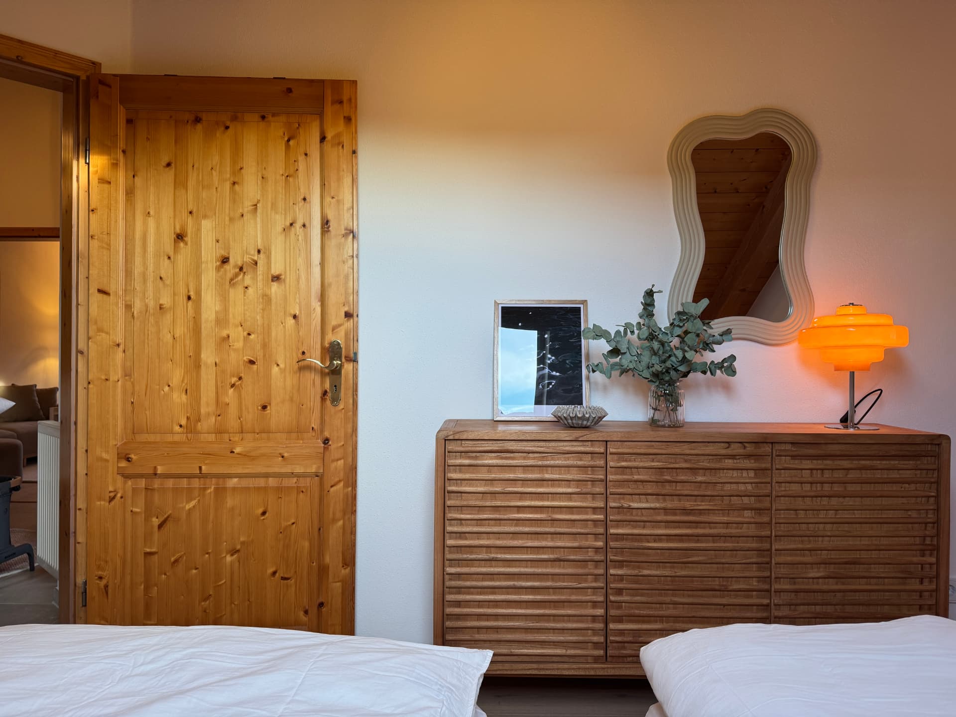Sideboard mit Wellenspiegel und oranger Vintage-Lampe im Schlafzimmer