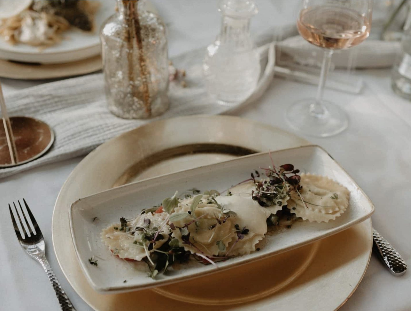 Fein angerichtete Ravioli mit Kräutern und ein Glas Wein in einem Restaurant am Chiemsee